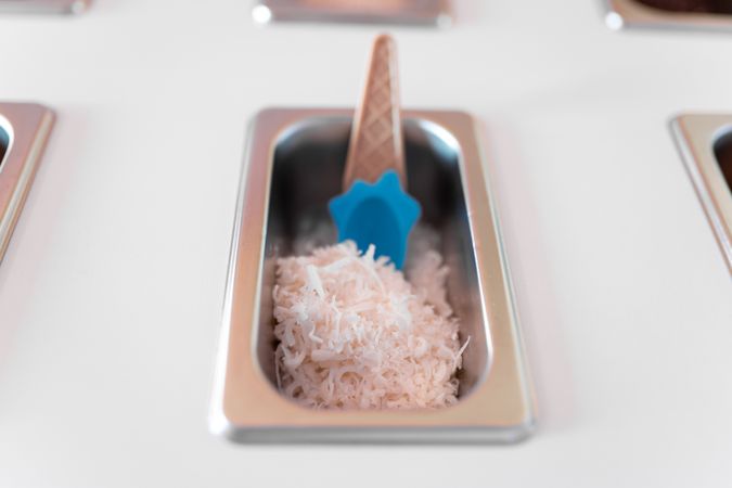 Close up photo of a metal tray filled with striped coconut toppings on an ice cream parlor counter