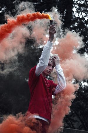 Man in red shirt and pants holding red smoke gun standing in the woods