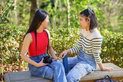 Two women sitting facing each other on outdoor bench in park