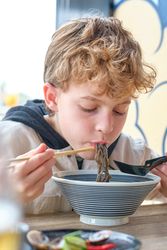 Hungry kid eating Japanese noodles from chopsticks
