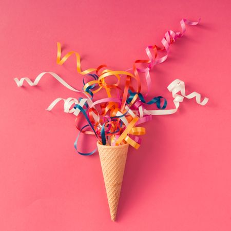 Ice cream cone with colorful party streamers on pink background
