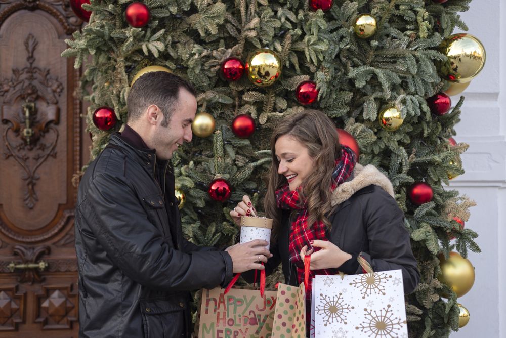 Happy young couple with paper bags standing near Christmas tree
