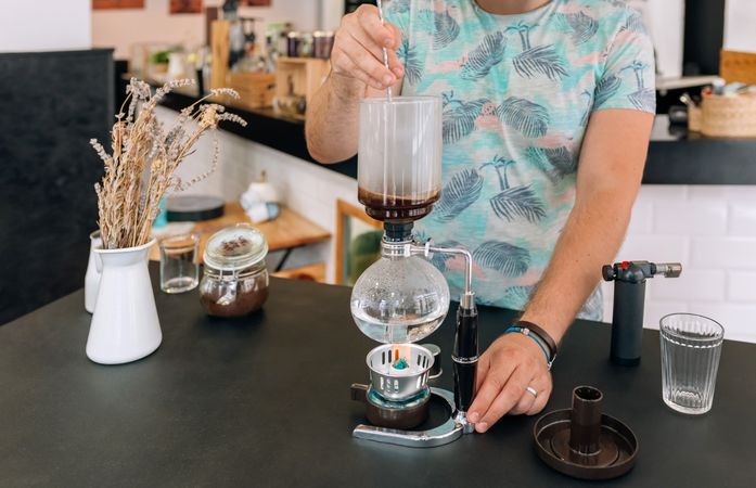 Barista skillfully stirring with spoon a specialty coffee into siphon of Japanese coffee maker