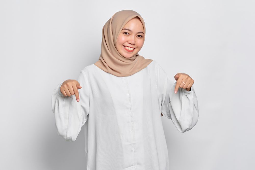 Smiling Asian female in headscarf with both fingers pointing to her feet