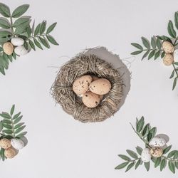 Nest with brown nest with green branches and brown eggs scattered on light  background