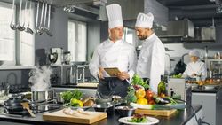 Two Famous Chefs Exchange Ideas About Video Blog Recipe they Watching on Tablet. They are Working in Big Restaurant Kitchen.