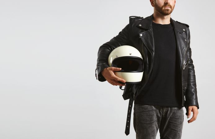Man in leather jacket holding motorcycle helmet on light background