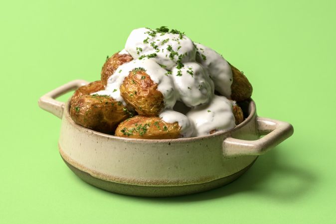 Baked potatoes with sour cream in a ceramic dish over a green background