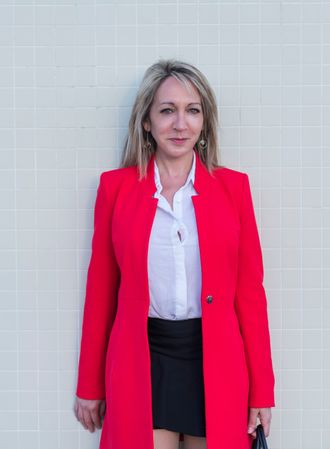 Portrait of a blonde woman wearing red jacket and skirt against a tiled wall