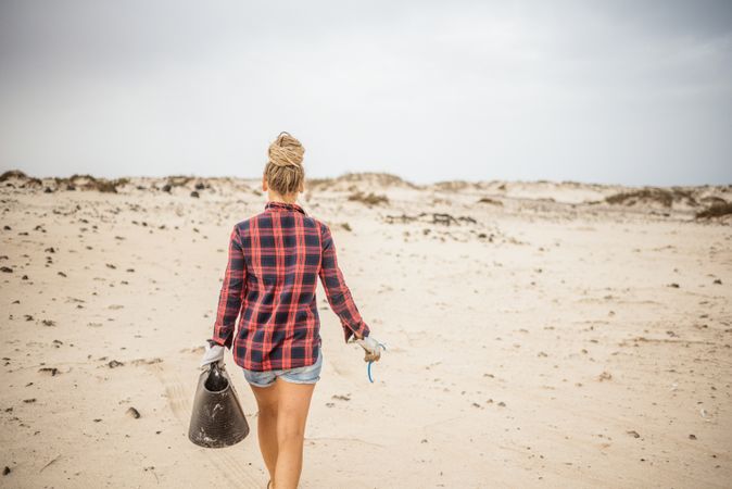 Content modern woman picking litter from sandy seashore