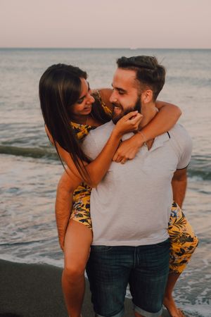 Amorous man carrying woman on arms along sandy beach