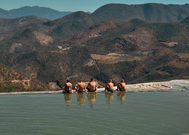 Backs of men and a woman enjoying view from natural mountain pool