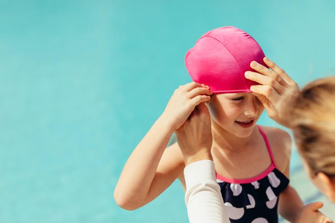 Female coach adjusting swimming cap on girl