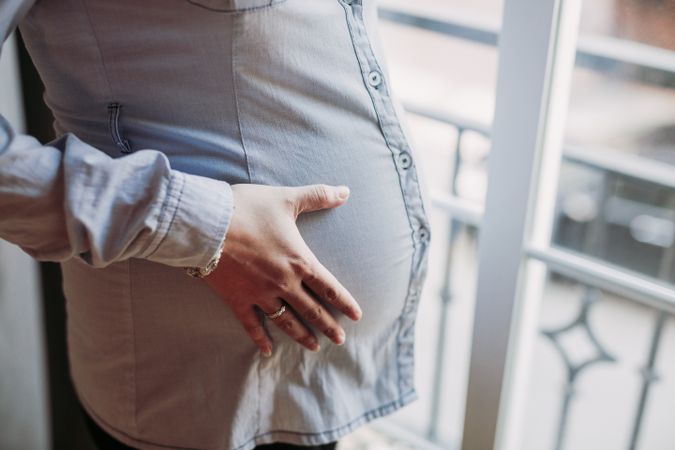 Pregnant woman looking at window at home