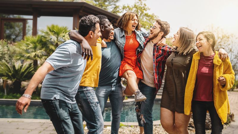Group of friends playfully lifting up a female friend