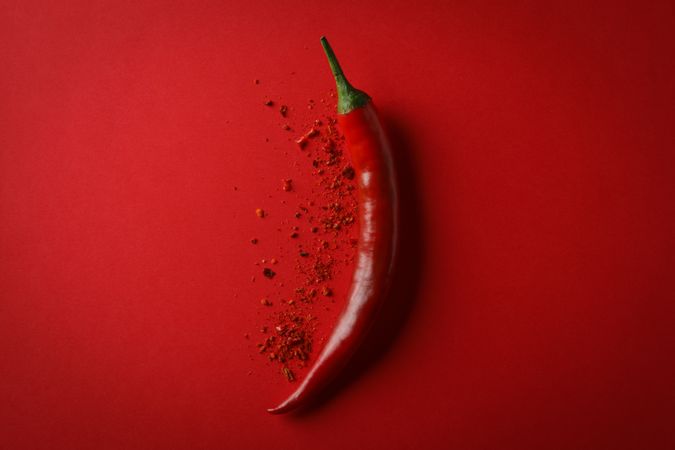 Tasty chilli pepper and powder spice on red background