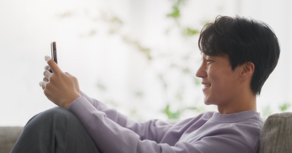 South Korean Young Man Enjoying His Leisure Time while Relaxing and Using a Smartphone.