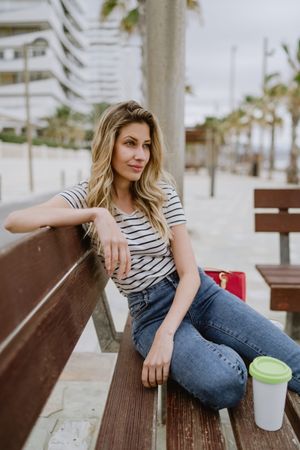 Happy woman with disposable cup of coffee sitting on street bench