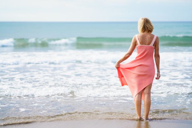 Back of mature woman standing on the beach facing the ocean, copy space