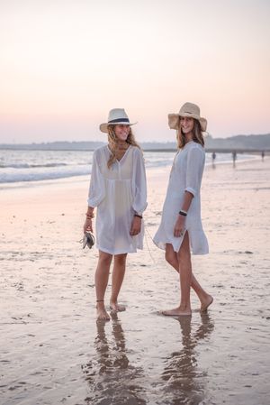 Smiling girlfriends in summer clothes barefoot in water on beach