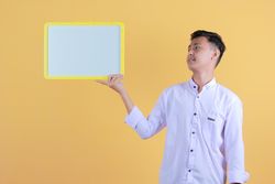 Portrait of a young man in yellow backdrop holding a blank note board