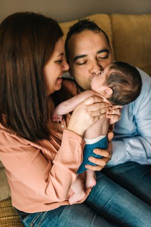Happy family sitting on couch together and father kissing baby.