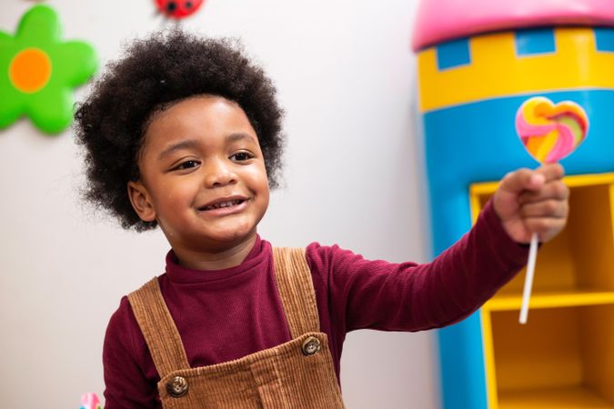 Small Black boy holding lollypop in play room