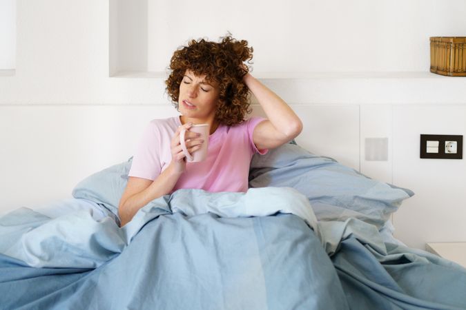 Woman waking up slowly in blue bed with cup of coffee
