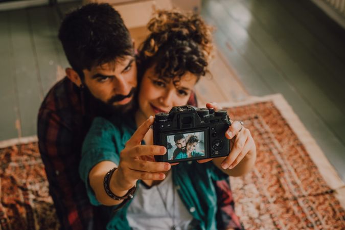Joyful couple embracing and taking selfie on camera at home