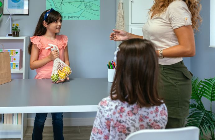 Student showing reusable mesh shopping bag to teacher in ecology classroom