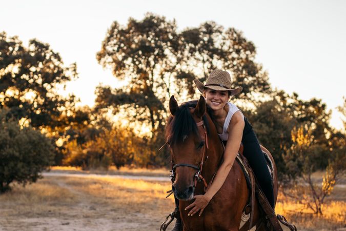 Young woman in hat riding a horse in the countryside at sunset