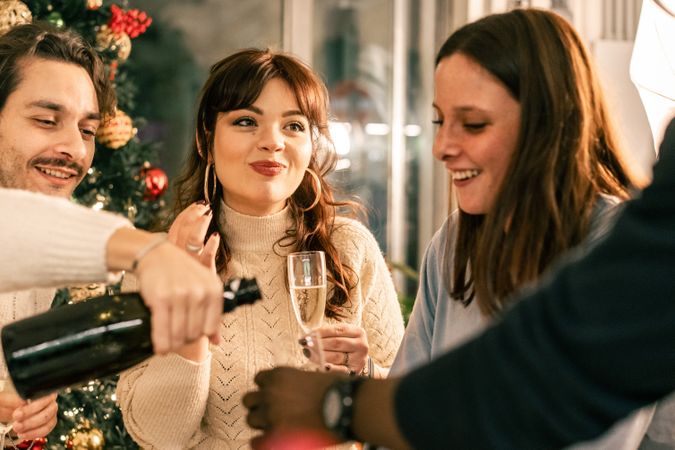 Young woman smiling and holding a glass of champagne at a Christmas dinner with friends.