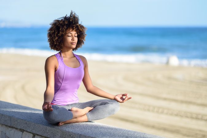Black woman with afro hairstyle meditating near the sea