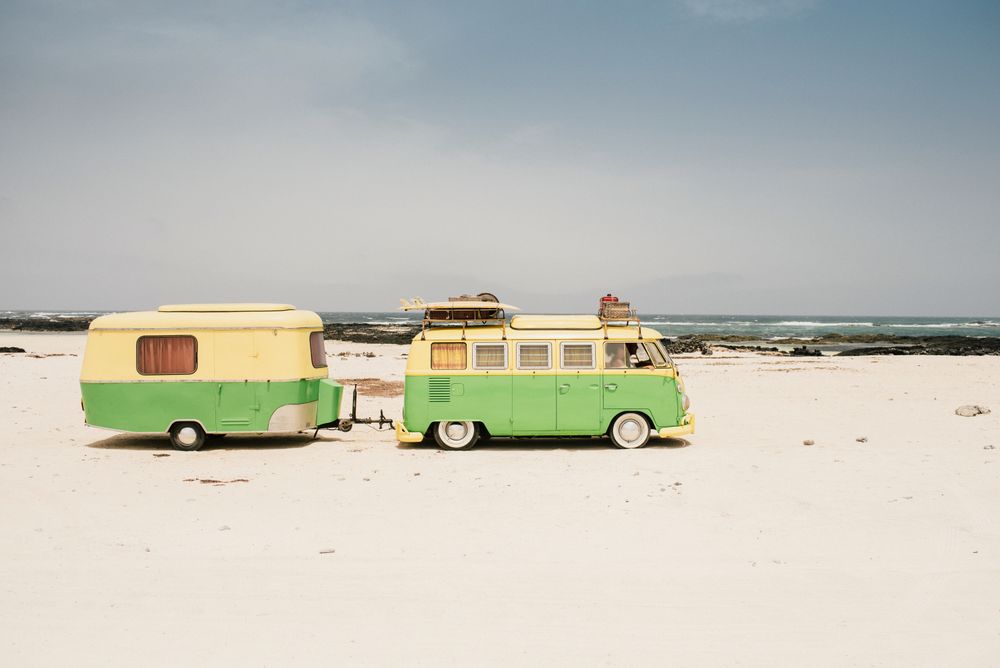 Colorful minibus with trailer parked on sandy shore in sunny day