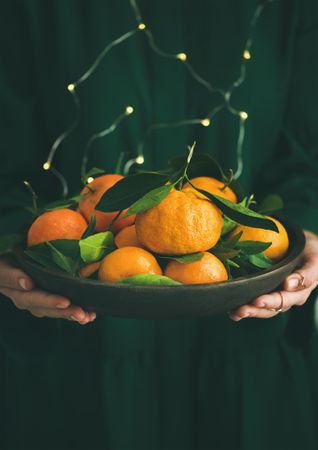Woman in green holding bowl of tangerines, with fairy lights, copy space