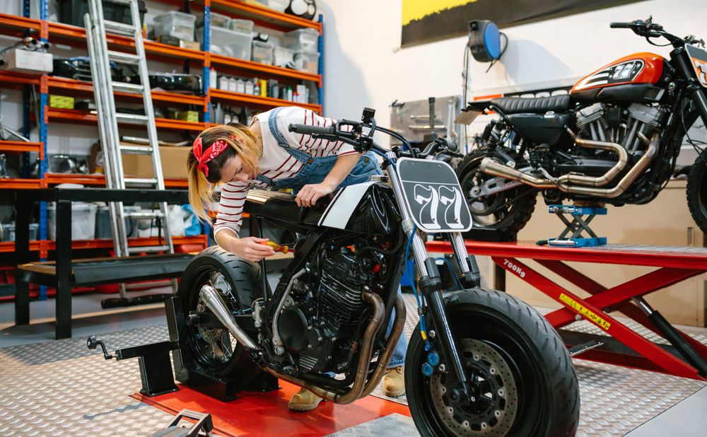 Mechanic woman repairing custom motorcycle on factory