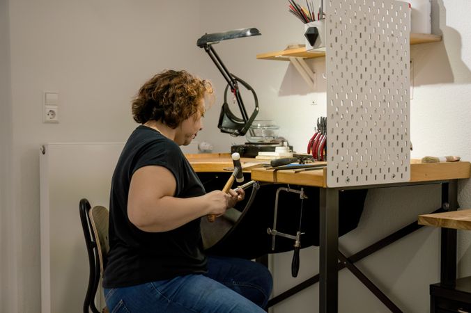 Focused adult craftswoman working in jewelry atelier.