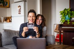 Happy female couple smiling with sonogram picture on video chat announcing their pregnancy