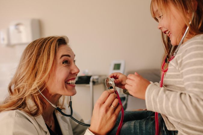 Friendly pediatrician playing with her girl patient with a stethoscope
