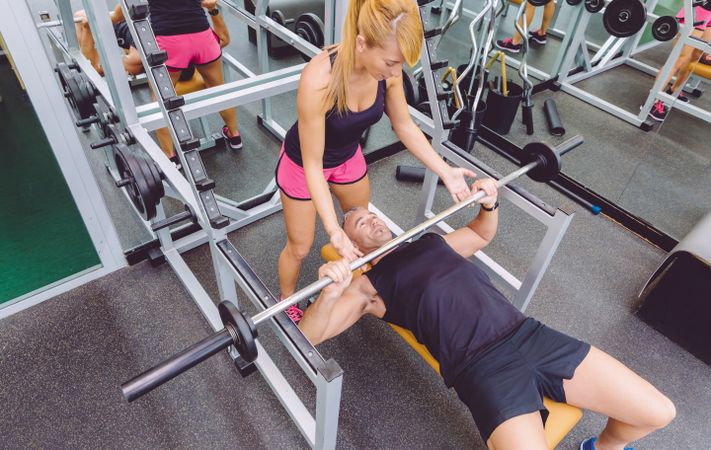 Fit female coach assisting client on bench press