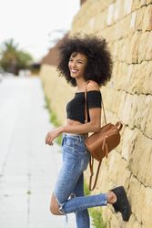 Smiling female standing on street with one leg up leaning on wall