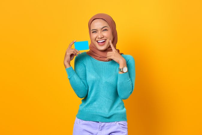 Muslim woman with finger on cheek while holding credit card