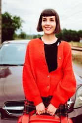 Smiling woman in red with suitcase nearby car