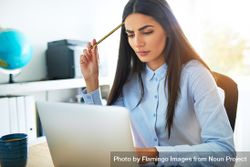 Pensive brunette woman in blue shirt working on laptop in office with pencil to head 0y3yq4