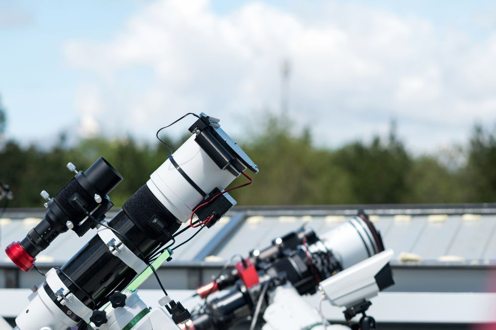 Telescopes on rooftop with cloudy sky background.