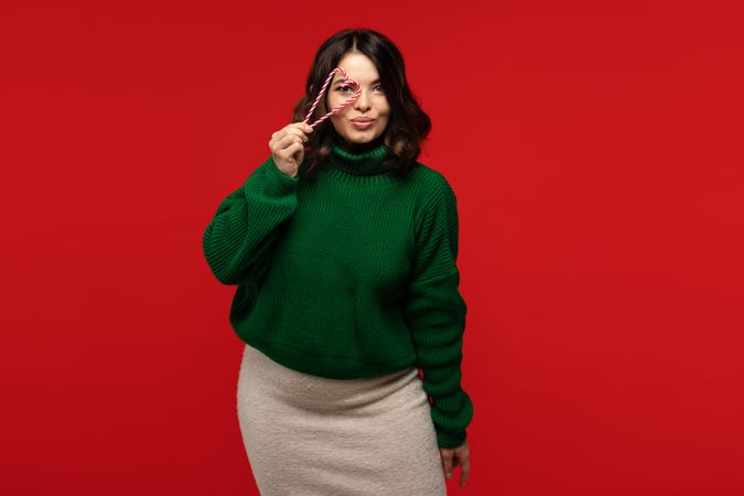 Woman in green sweater playfully looking through heart-shaped candy cane