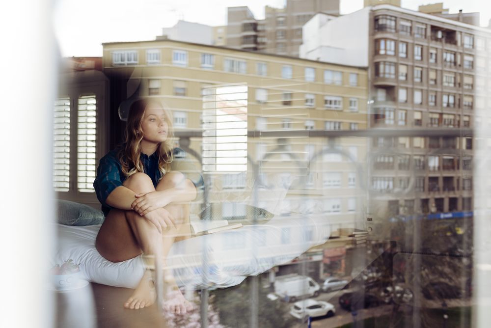 Young female sitting on bed and looking trough window