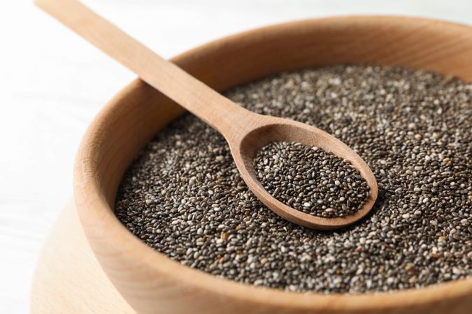 Wooden bowl with chia and spoon on wooden background, close up