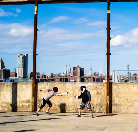 Two people fencing in Brooklyn Bridge Park, with the Empire State Building in the distance