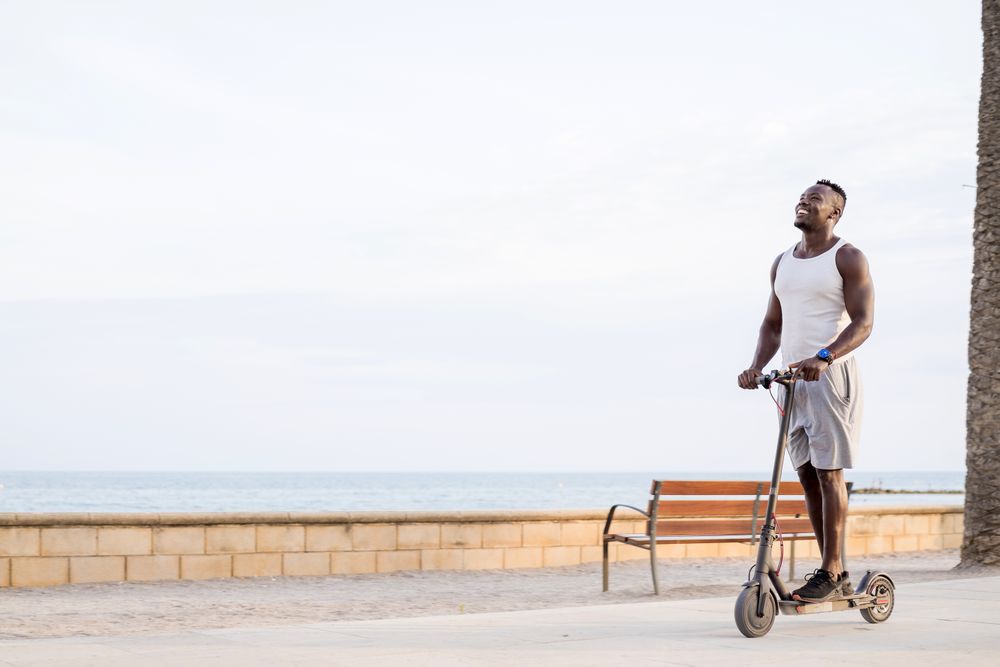 Cool adult Black man riding scooter in street
